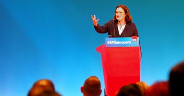 Andrea Nahles am SPD-Redepult vor blauem Hintergrund macht eine greifende Geste